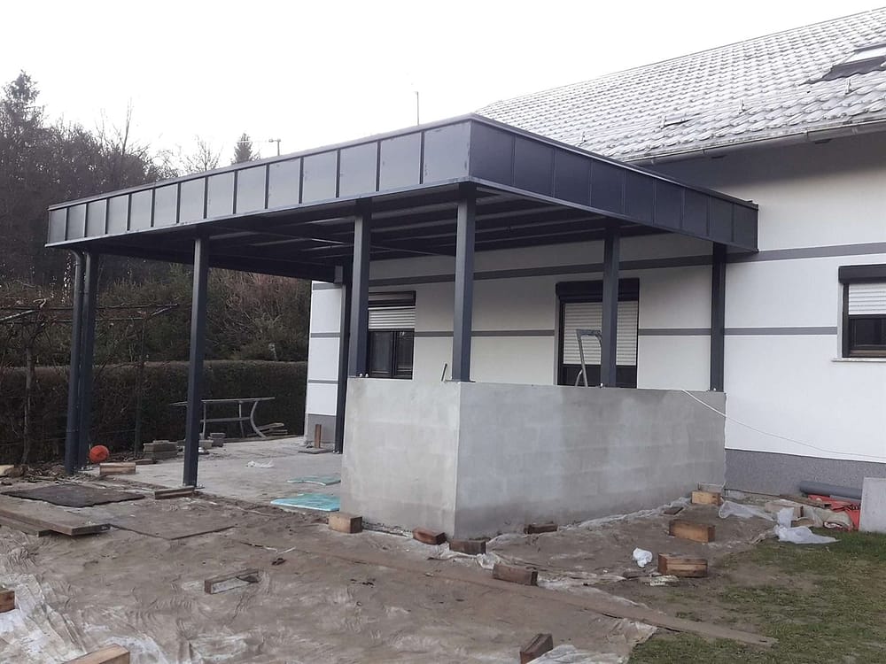 Kovinski nadstrešek s temno obrobo ob stanovanjski hiši, med izvedbo