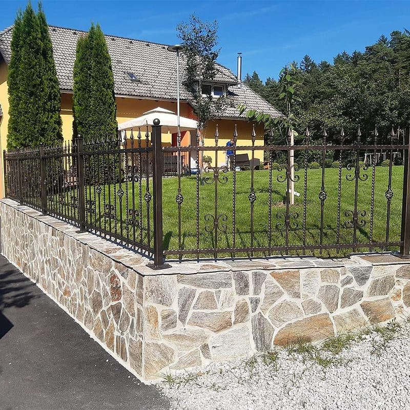 Kovinska ograja s kovanimi okraski na kamnitem zidcu ob hiši